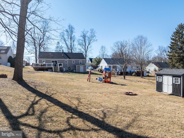 view of yard featuring a wooden deck, an outdoor fire pit, a playground, and a storage unit