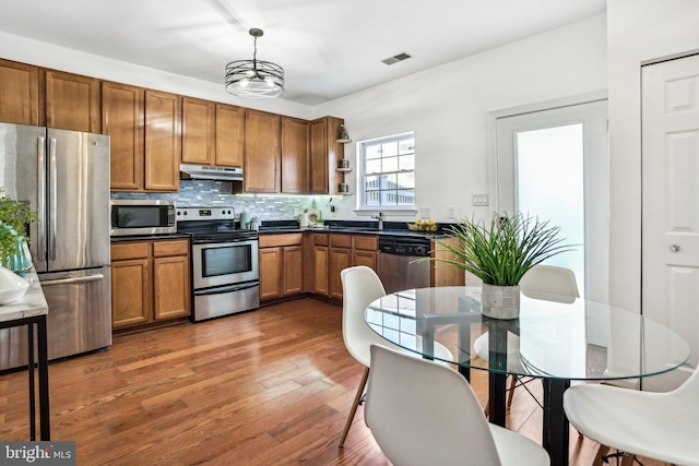 kitchen with dark wood-type flooring, an inviting chandelier, hanging light fixtures, stainless steel appliances, and tasteful backsplash