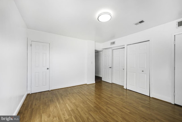 unfurnished bedroom featuring baseboards, visible vents, dark wood finished floors, and two closets