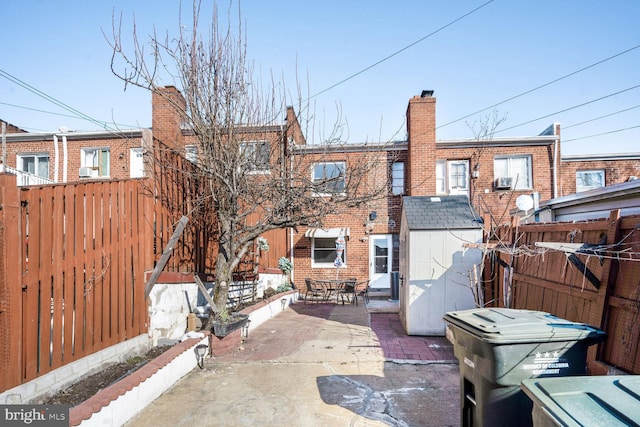 rear view of property with a patio, a storage shed, brick siding, fence, and a chimney