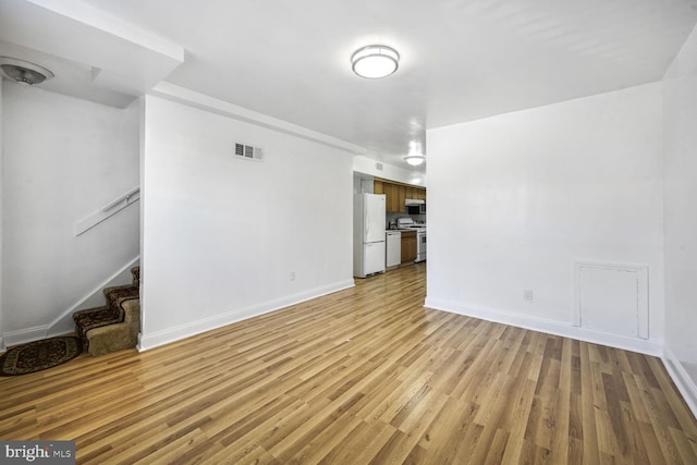 unfurnished living room with baseboards, stairway, visible vents, and light wood-style floors