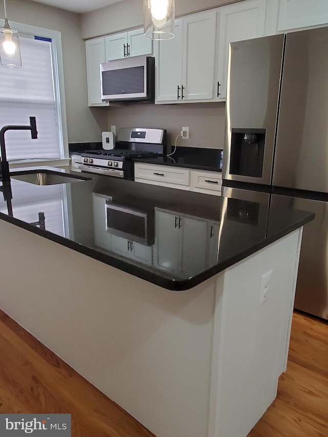 kitchen with sink, white cabinetry, hanging light fixtures, stainless steel appliances, and light wood-type flooring