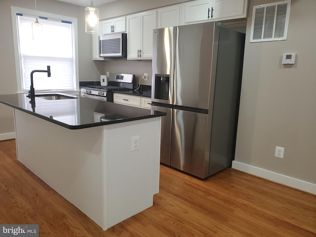 kitchen featuring sink, white cabinets, hanging light fixtures, light hardwood / wood-style floors, and stainless steel appliances