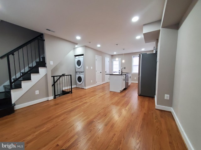 unfurnished living room featuring stacked washing maching and dryer, sink, and light hardwood / wood-style floors