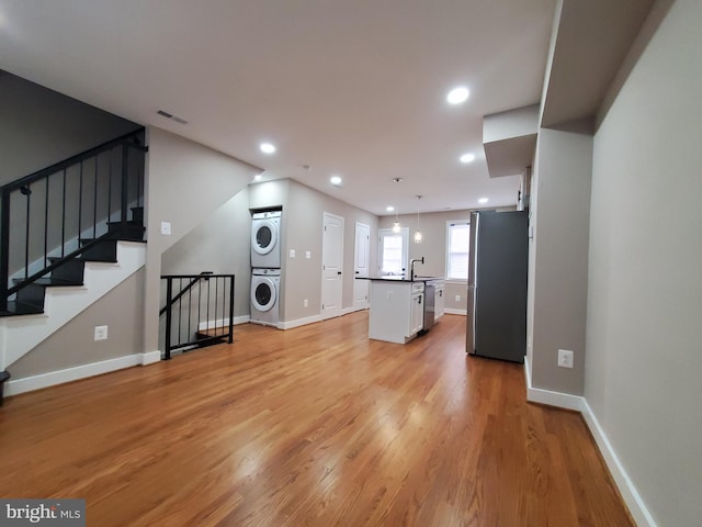 unfurnished living room featuring stacked washer and dryer, sink, and light wood-type flooring