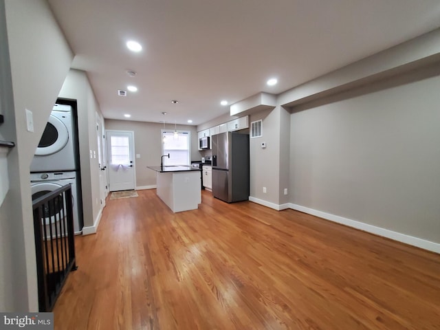 kitchen with appliances with stainless steel finishes, stacked washer / dryer, a kitchen island, decorative light fixtures, and light wood-type flooring