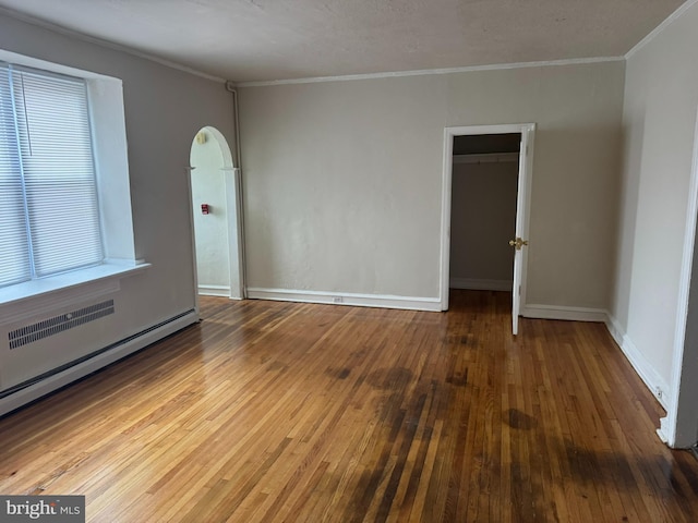 empty room featuring hardwood / wood-style floors, a baseboard heating unit, baseboards, and ornamental molding