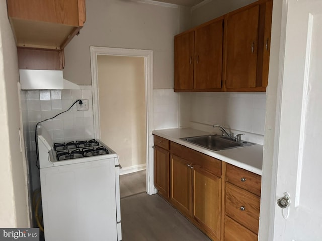 kitchen with brown cabinetry, light countertops, white range with gas stovetop, and a sink