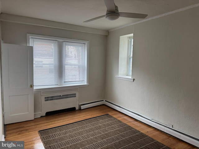 unfurnished room with radiator, wood finished floors, plenty of natural light, and a baseboard radiator