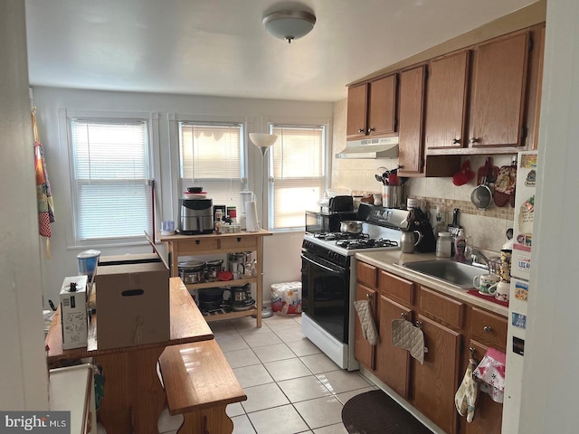 kitchen featuring light tile patterned flooring, decorative backsplash, sink, and range with gas cooktop