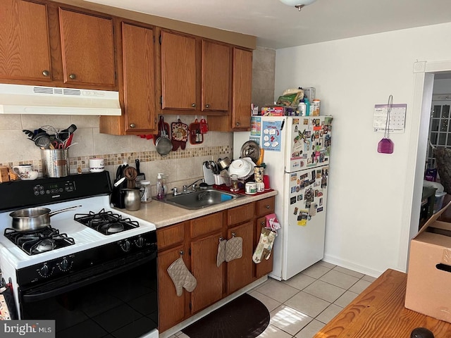 kitchen featuring sink, gas range, tasteful backsplash, light tile patterned floors, and white fridge