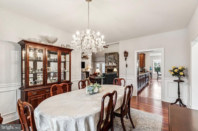 dining space with a stone fireplace, a healthy amount of sunlight, an inviting chandelier, and dark hardwood / wood-style flooring