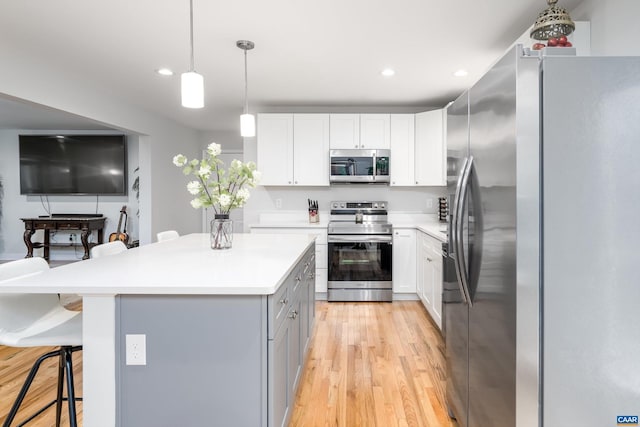 kitchen featuring a kitchen island, a breakfast bar, white cabinetry, hanging light fixtures, and stainless steel appliances