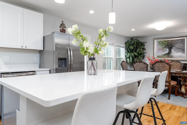 kitchen featuring a breakfast bar, hanging light fixtures, stainless steel appliances, light hardwood / wood-style floors, and white cabinets