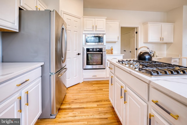 kitchen with appliances with stainless steel finishes, light stone countertops, light wood-type flooring, and white cabinets