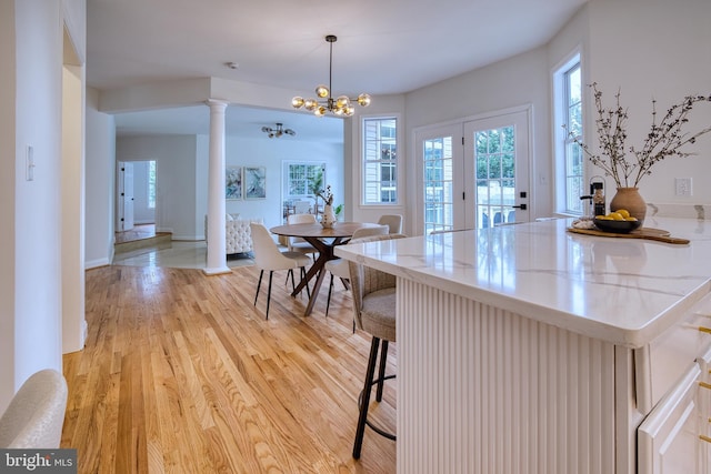 dining space with decorative columns, a chandelier, and light hardwood / wood-style flooring