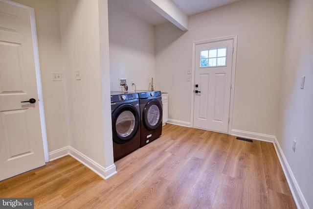 clothes washing area featuring separate washer and dryer, light hardwood / wood-style flooring, and cabinets