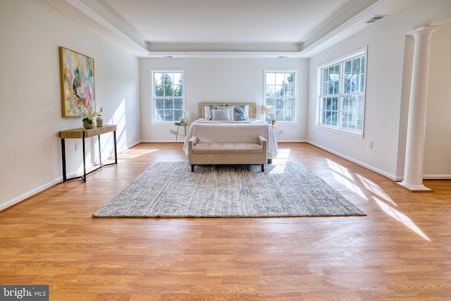 bedroom with a tray ceiling, light hardwood / wood-style floors, and ornate columns