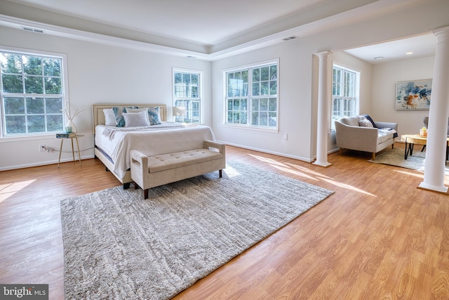 bedroom featuring light hardwood / wood-style flooring, a raised ceiling, and ornate columns