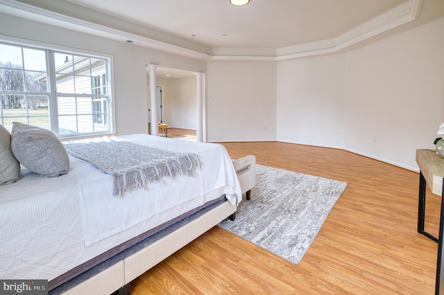 bedroom featuring ornate columns, ornamental molding, a tray ceiling, and light wood-type flooring