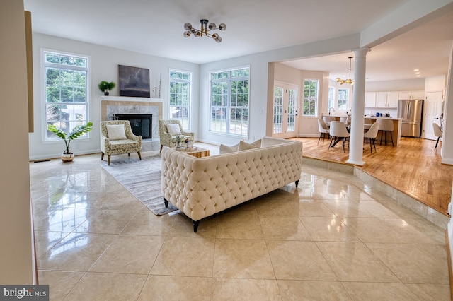 living room with light tile patterned floors, a fireplace, a chandelier, and ornate columns