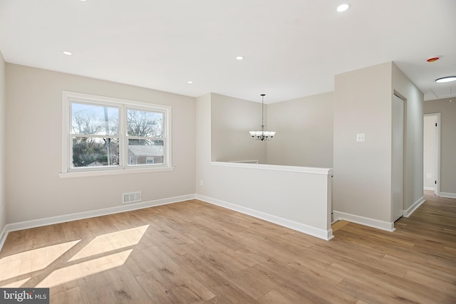 spare room with an inviting chandelier and light hardwood / wood-style flooring