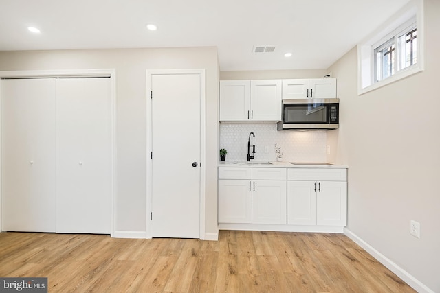 kitchen with sink, white cabinets, backsplash, and light hardwood / wood-style flooring