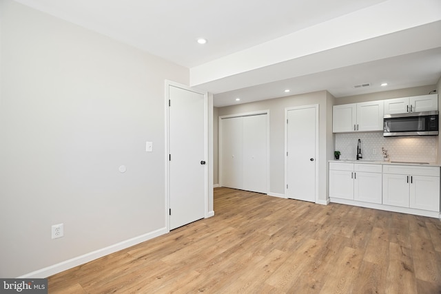 kitchen with sink, white cabinetry, light wood-type flooring, black electric stovetop, and backsplash