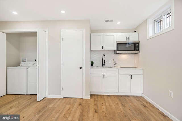 kitchen featuring sink, light hardwood / wood-style flooring, backsplash, independent washer and dryer, and white cabinets