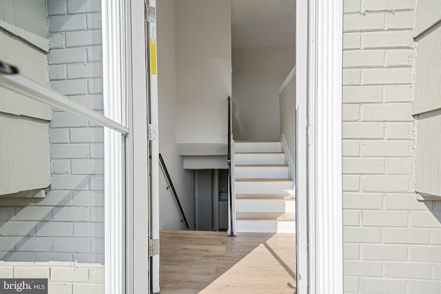stairway with hardwood / wood-style floors and brick wall