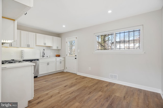 kitchen with sink, light wood-type flooring, appliances with stainless steel finishes, decorative backsplash, and white cabinets