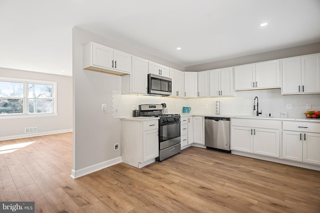 kitchen with white cabinetry, stainless steel appliances, sink, and light hardwood / wood-style flooring