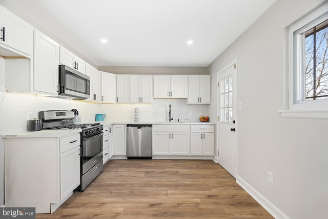 kitchen featuring sink, white cabinetry, stainless steel appliances, light hardwood / wood-style floors, and decorative backsplash