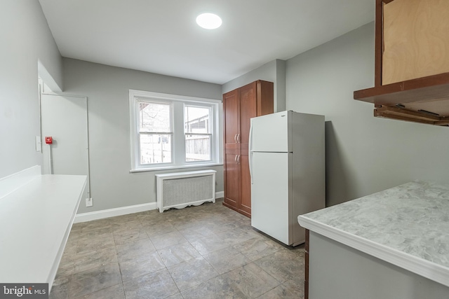 kitchen featuring radiator heating unit, baseboards, light countertops, freestanding refrigerator, and brown cabinetry