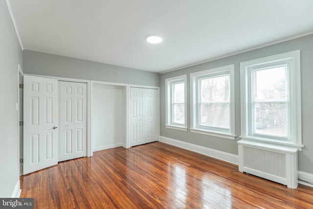 unfurnished bedroom featuring baseboards, dark wood-type flooring, multiple closets, and radiator