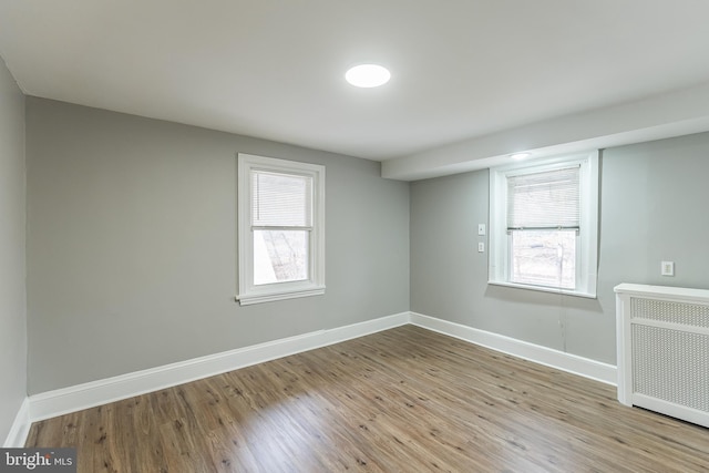 spare room featuring baseboards, plenty of natural light, light wood finished floors, and radiator heating unit