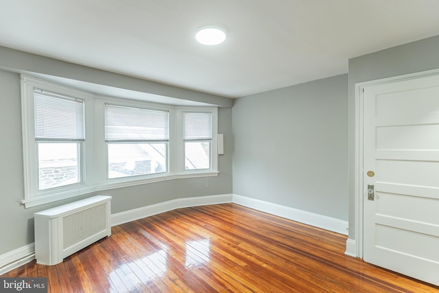 unfurnished room featuring radiator, baseboards, and wood finished floors