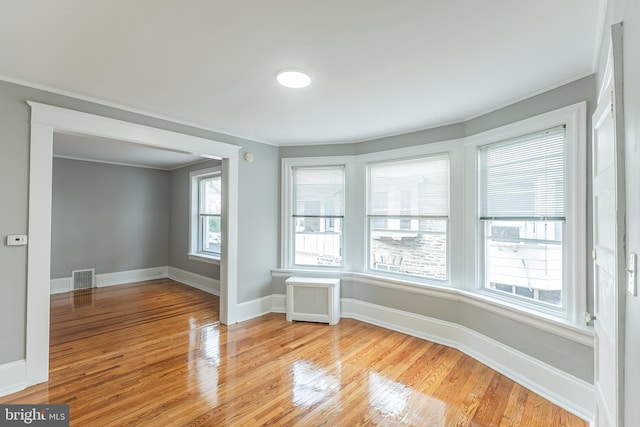 unfurnished room featuring baseboards, light wood-style floors, visible vents, and radiator