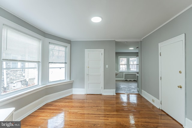 empty room with light wood-style floors, radiator, ornamental molding, and baseboards