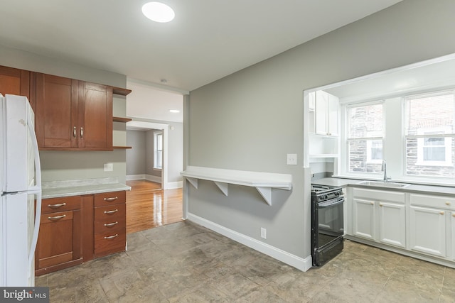 kitchen featuring a sink, black gas stove, light countertops, freestanding refrigerator, and open shelves