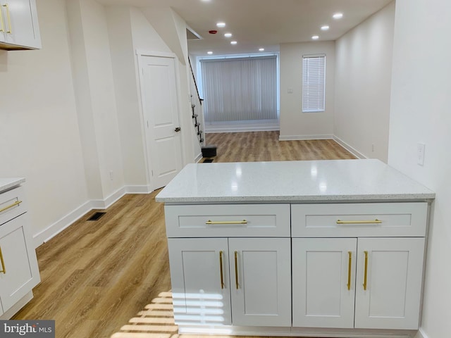 kitchen with light stone counters, white cabinetry, and light hardwood / wood-style flooring