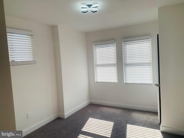 spare room with a wealth of natural light and dark carpet