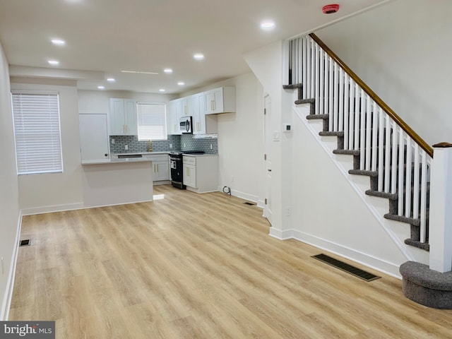 kitchen with black electric range oven, light hardwood / wood-style flooring, kitchen peninsula, and white cabinets