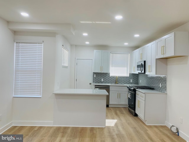 kitchen featuring sink, appliances with stainless steel finishes, white cabinetry, backsplash, and light hardwood / wood-style floors