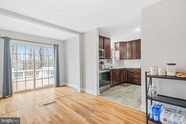 kitchen with backsplash, appliances with stainless steel finishes, dark brown cabinets, and light hardwood / wood-style floors