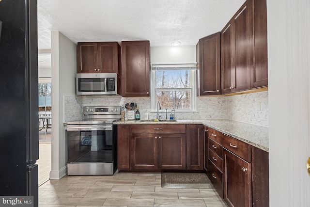 kitchen featuring appliances with stainless steel finishes, sink, a textured ceiling, light stone countertops, and tasteful backsplash