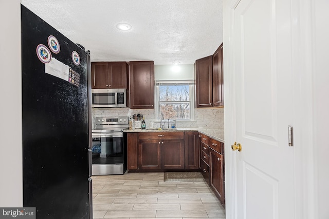 kitchen with sink, tasteful backsplash, light stone counters, a textured ceiling, and appliances with stainless steel finishes