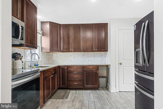 kitchen with appliances with stainless steel finishes, sink, backsplash, light stone counters, and light hardwood / wood-style flooring