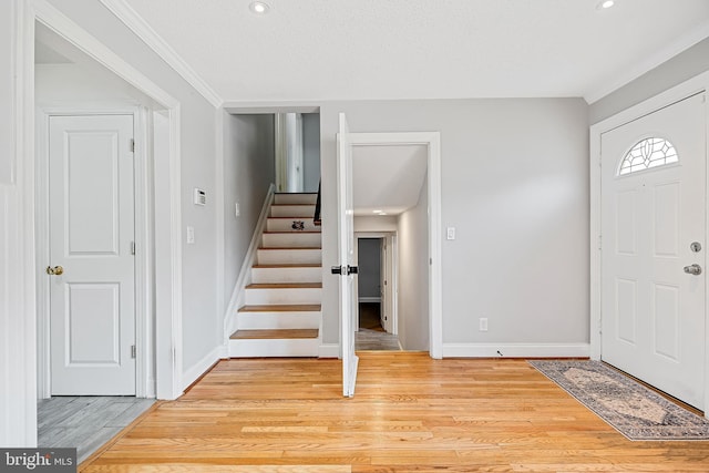 entryway with light wood-type flooring, crown molding, and a textured ceiling