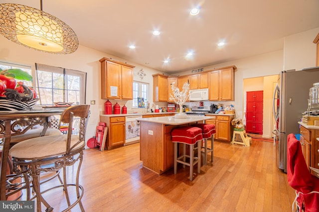 kitchen featuring appliances with stainless steel finishes, hanging light fixtures, a kitchen island, and light wood-type flooring